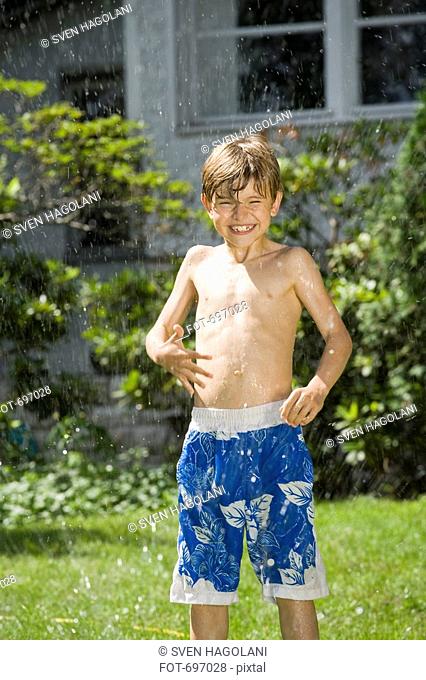 A young boy standing in a sprinkler