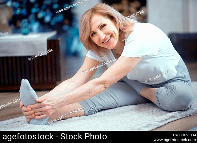 Concetrated Woman Stretches Her Feet Touching Her Feet. Mature Woman Does Yoga Exersice Reaching For Her Toes. Healthy Lifestyle. Stretching