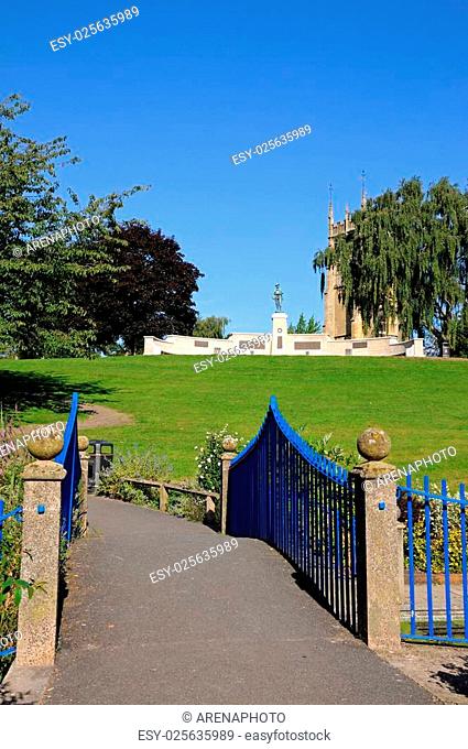 View across footbridge towards the Evesham War Memorial in Abbey Gardens with the Abbey clock tower to the rear, Evesham, Worcestershire, England, UK