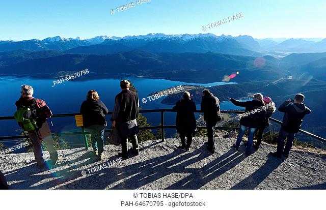 Mountain hikers stand on the viewing plattform on the mountain peak of the Herzogstand enjoying the warm sun near lake Walchensee, Germany, 26 December 2015