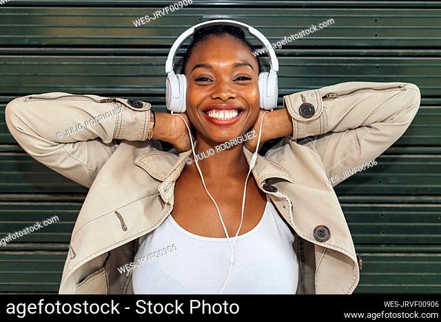 Cheerful woman wearing headphones while listening music in front of shutter