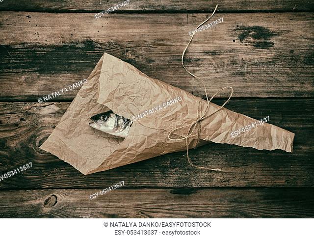 Fresh whole sea bass fish wrapped in a brown paper and tied with a rope, wooden table, top view