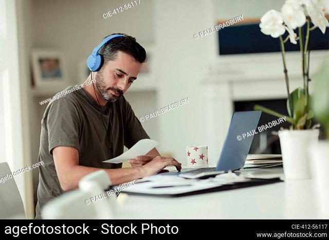 Man with headphones and receipts paying bills at laptop