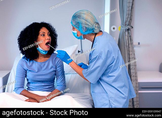 African american female patient with mouth open tested with swab test by female doctor in face mask