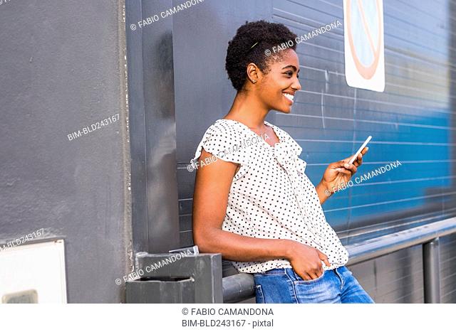 African American woman leaning on railing texting on cell phone