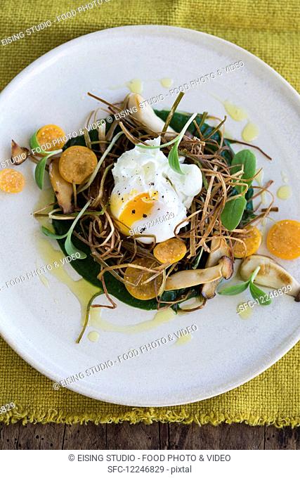 A poached egg on fried leeks with spinach puree, herbs, kumquats and borage shoots