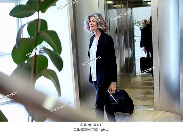 Senior businesswoman with wheeled suitcase in office building