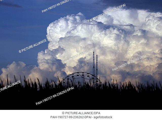 27 July 2019, Bavaria, Kirchheim: Clouds pile up shortly before sunset over the rides of the amusement park ""Skylinepark""