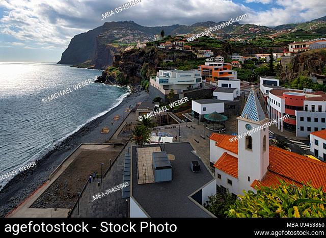 View over beach and Nossa Senhorada Conceicao church on the coast to the cliffs of Cabo Girao, Camara de Lobos, Madeira island, Portugal