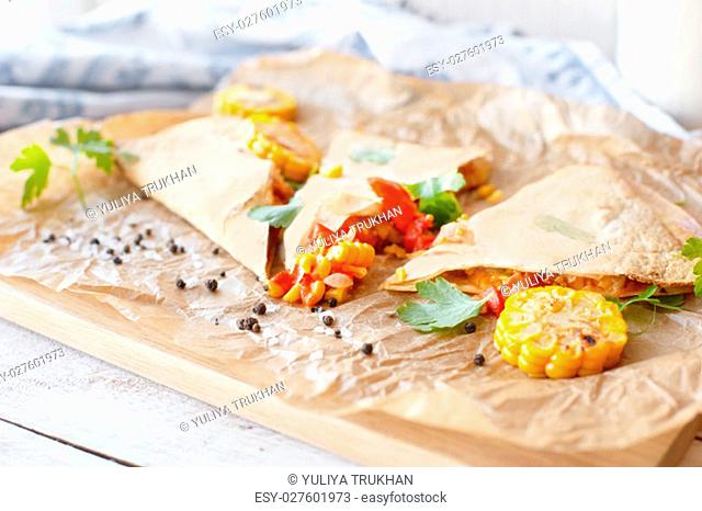Mexican Quesadilla wrap with vegetables, corn, sweet pepper and sauces on the parchment and table. horizontal view