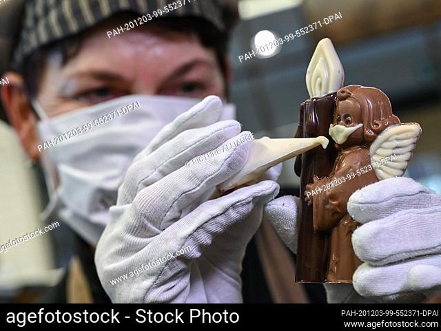 02 December 2020, Brandenburg, Hornow: Anne Walter, chocolatier from the Confiserie Felicitas, uses liquid white chocolate to decorate a small Christmas figure...