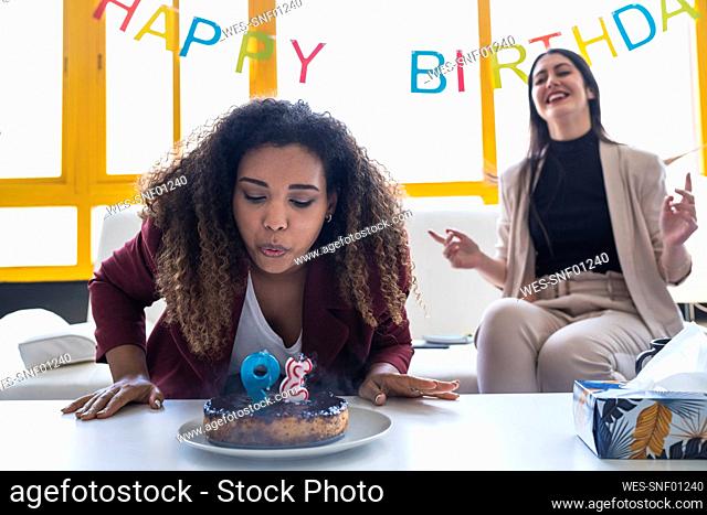 Female professional blowing birthday candle on cake during celebration at coworking office