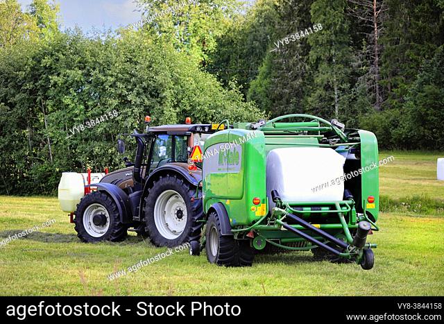 Farmer working in hay field with Valtra tractor and McHale 3 plus integrated baler wrapper. Salo, Finland. August 28, 2020