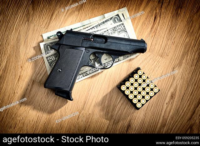 Image of a pistol with cartridges and dollar notes on a wooden table