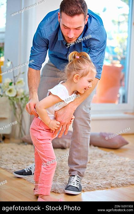 Vater hilft seiner Tochter beim Hose anziehen zu Hause