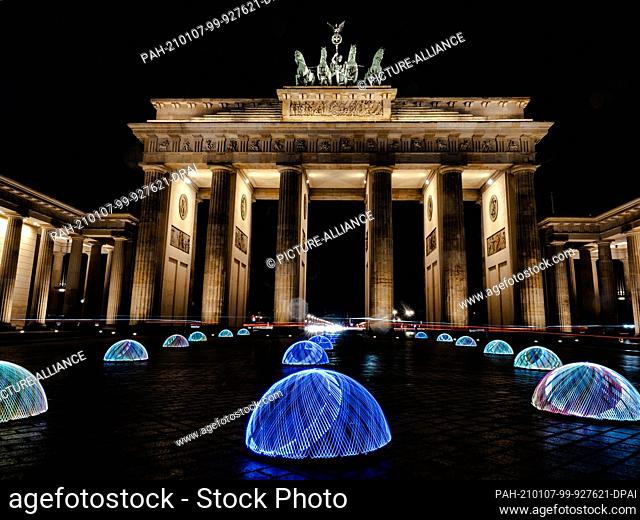 06 January 2021, Berlin: A man has drawn numerous hemispheres on the Pariser Platz in front of the Brandenburg Gate with a wheel equipped with LED lights