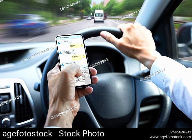Close-up Of A Man's Hand Typing Text Message On Mobile Phone While Driving Car