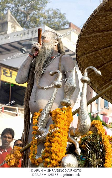 Hindu saint naga baba Shivdasgiri with trishul smoking tobacco ; Varanasi on Ganga river ; Uttar Pradesh ; India MR707A