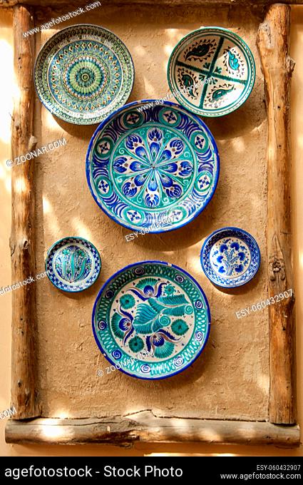 eastern ceramic plates hang on a clay wall. the wall of clay is decorated in an oriental style with a ceramic plate and wooden blocks