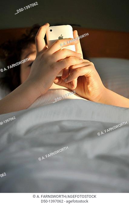 10 year old boy playing games on his iPhone while in bed, Zakopane, Poland