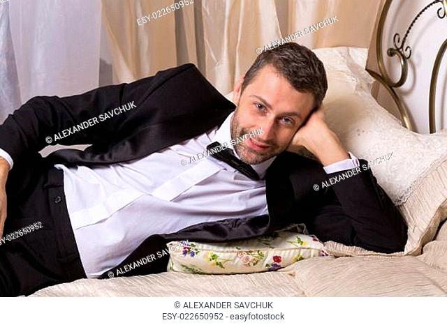 Elegant playboy reclining on a bed