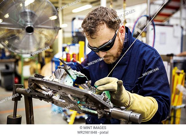 Male skilled factory worker wearing eye protectors welding a bicycle part in a factory
