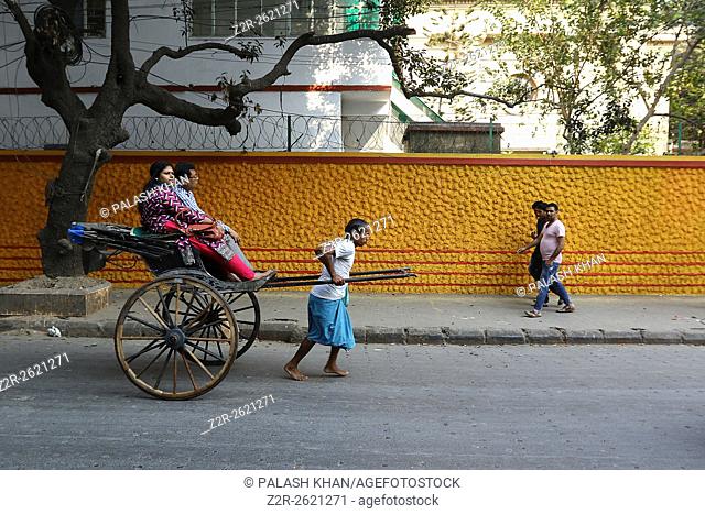 India, 19 February 2016. Hand pulling rickshaw puller pulling with passenger walks past a colorful wall at street of Kolkata