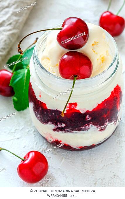 Glass jar with ice cream and sweet cherry on white concrete background