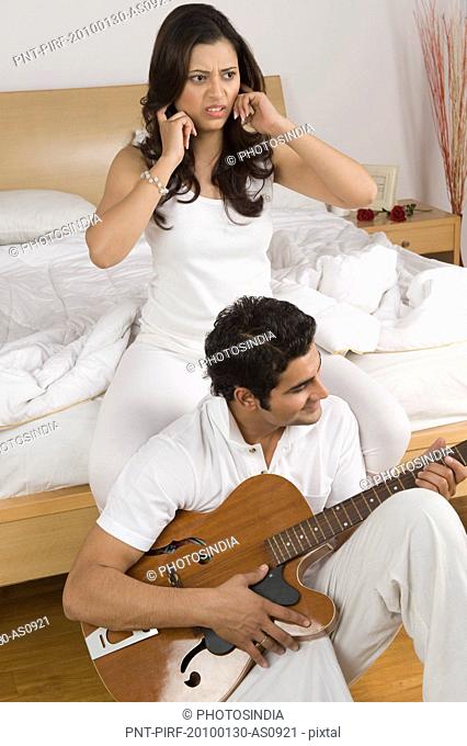 Man playing a guitar with his wife putting fingers in ears