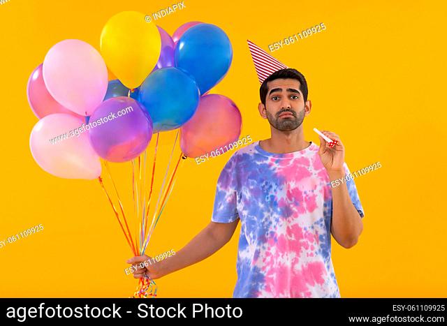 Portrait of sad young man holding balloons and party horn in hands