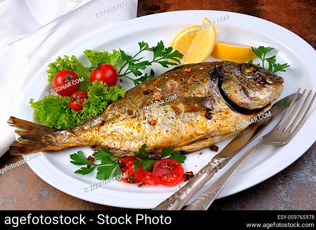 roasted fish Dorado with vegetables garnish and lemon slices on a plate
