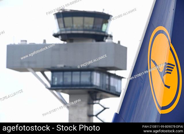 10 August 2021, Brandenburg, Schšnefeld: The logo on the tail unit of a Lufthansa aircraft can be seen against the backdrop of the tower at Berlin Brandenburg...