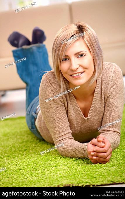 Portrait of attractive blond woman lying on floor at home, looking at camera, smiling
