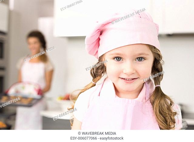 Little girl wearing pink apron and chefs hat smiling at camera