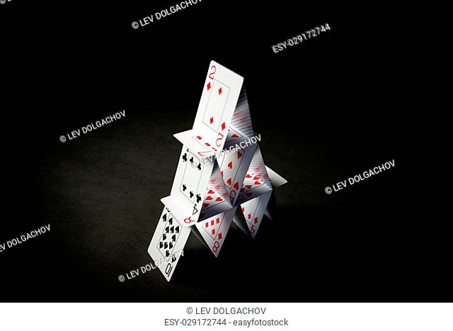 casino, gambling, games of chance, hazard and insecurity concept - house of playing cards over black background
