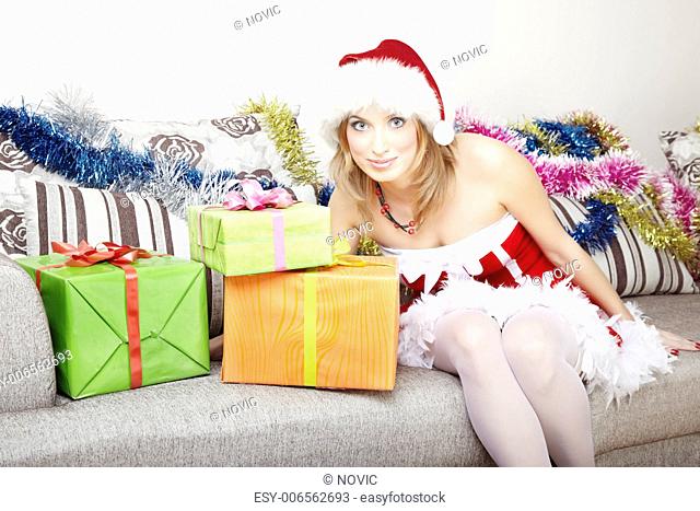 Smiling lady in Santa Claus costume sitting indoors near the Christmas gifts