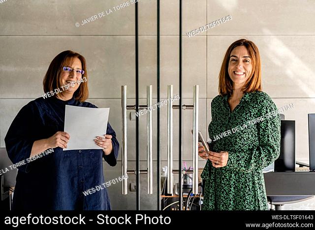 Smiling female colleagues standing by glass door in cabin