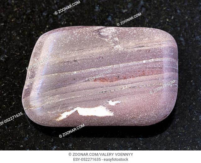 macro shooting of natural mineral rock specimen - polished Argillite gemstone on dark granite background from Sundozero region on Karelia, Russia