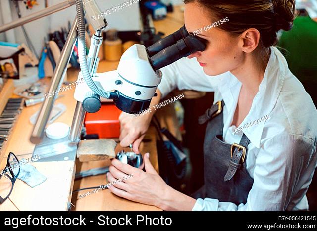 Diligent jeweler working on microscope at her workbench on some jewelry