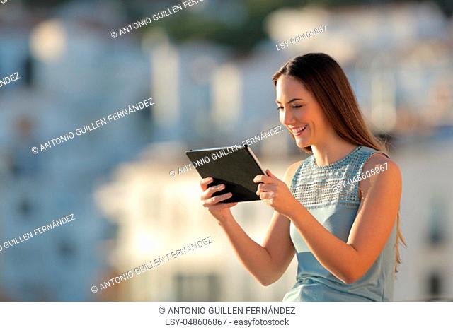 Happy woman is watching media content on a tablet in a town at sunset