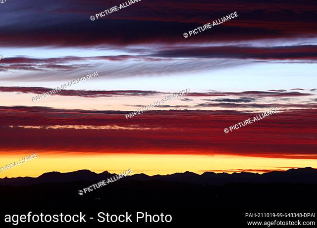 19 October 2021, Bavaria, Bernbeuren: The sky above the panorama of the Alps turns different shades of red shortly before sunrise