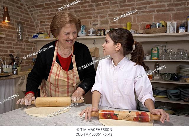 Grandmother and granddaughter 9-11 rolling pastry in kitchen