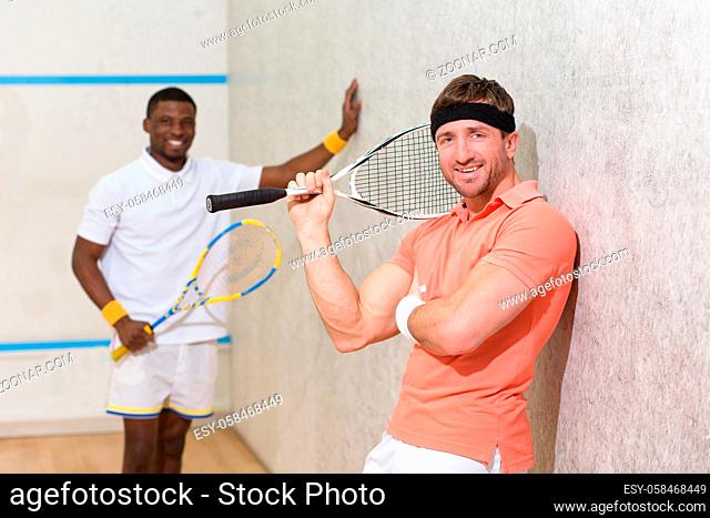 Portrait of two handsome men posing for camera after playing squash on court. Happy friends spending their weekends doing sports