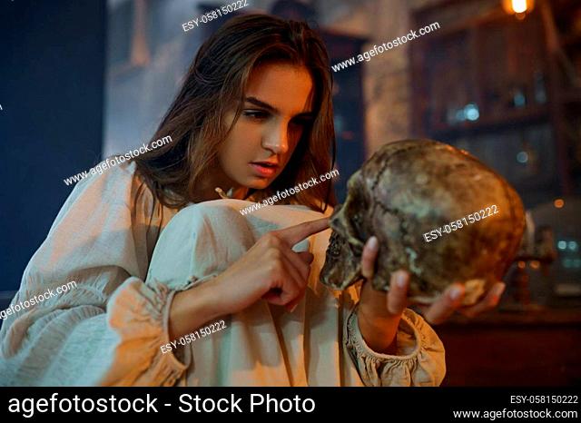 Scary demonic woman holds human skull, demons casting out. Exorcism, mystery paranormal ritual, dark religion, night horror, potions on shelf on background