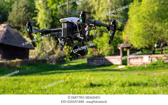 Flying copter with raised chassis and a camera is filming in the countryside. Photographed close-up with the bottom point