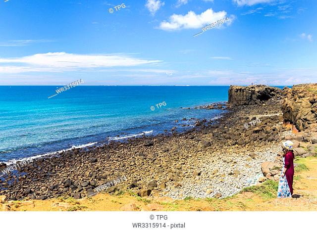 Girl in red.Blue ocean and sky with white cloud beside the coast;hale Cave;Xiaomenyu;Penghu;Taiwan
