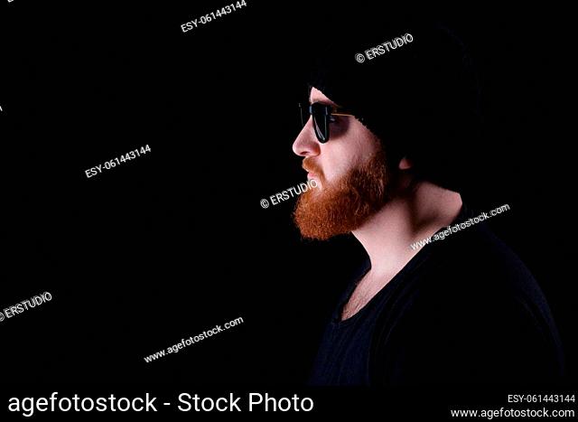 profile of red bearded man in sunglasses and hat on black background