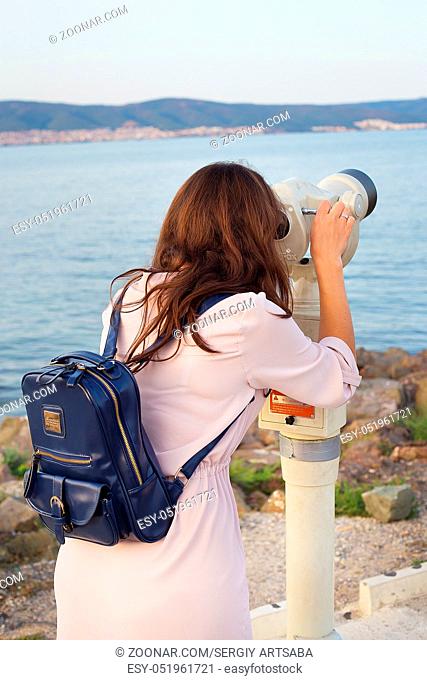 The girl looks through the telescope at the sea