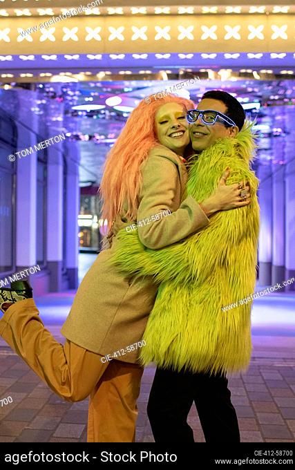 Portrait happy stylish couple hugging under neon lights on sidewalk