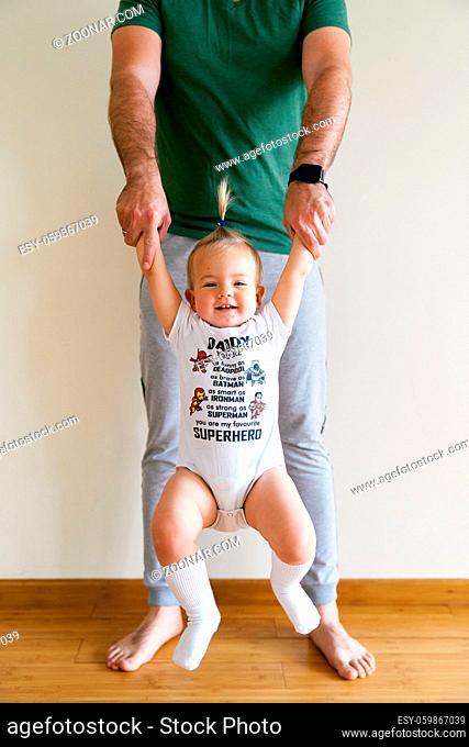 Little girl swinging on daddy's arms in the room. High quality photo